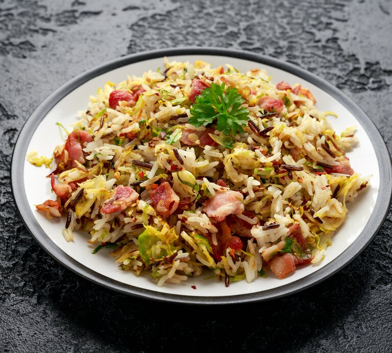 Ein Teller mit Rosenkohl-Bratreis mit Speck auf einem dunklen Untergrund. | © Shutterstock/DronG