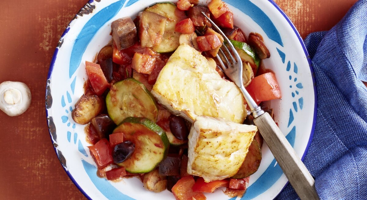 Auf einem Teller ist eine Portion Ratatouille mit Fisch aus der französischen Küche angerichtet.