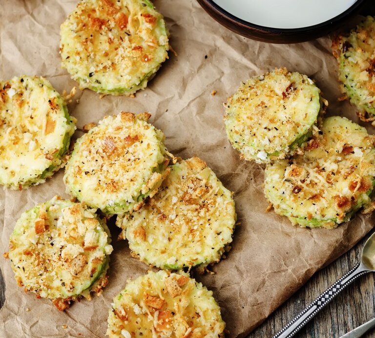 Zucchini-Parmesan-Chips auf einem Backpapier. Daneben Besteck und ein Ausschnitt einer Schale. | © Getty Images/ nata_vkusidey