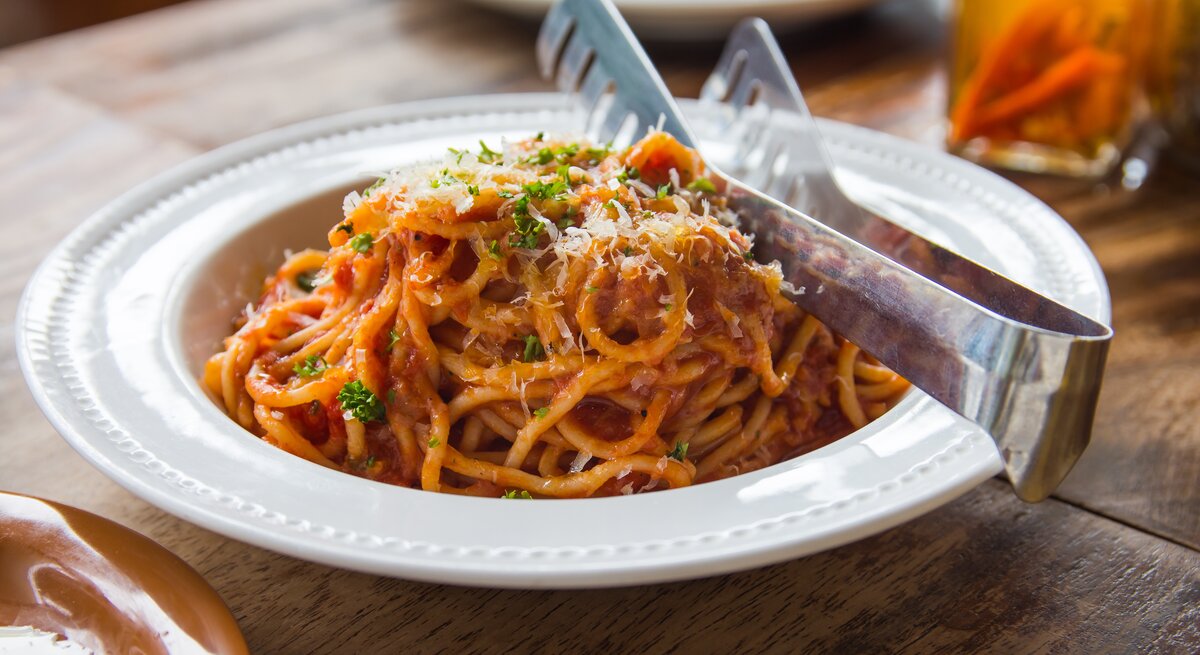 Das Bild zeigt einen Teller mit Spaghetti in einer Thunfisch-Bolognese, bestreut mit geriebenem Käse und etwas gehackter Petersilie. 