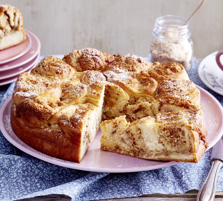 Ein Dänischer Butterkuchen steht auf einem Tisch. Daneben liegen mehrere Teller, ein Messer sowie eine Tasse mit einem Unterteller. | © EAT CLUB / Isabell Triemer