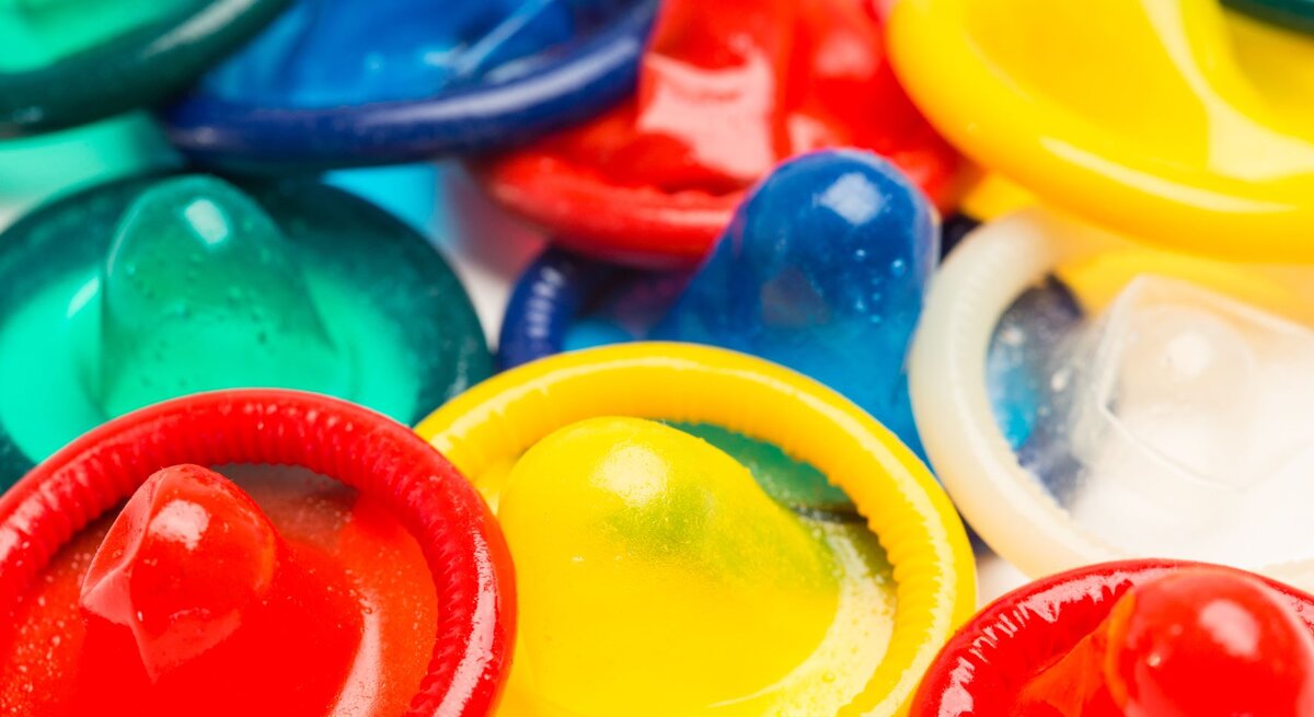 Nahaufnahme mehrerer Kondome in verschiedenen Farben wie Rot, Gelb, Grün und Blau. Sie sind in einer unregelmäßigen Anordnung auf einem Haufen platziert.