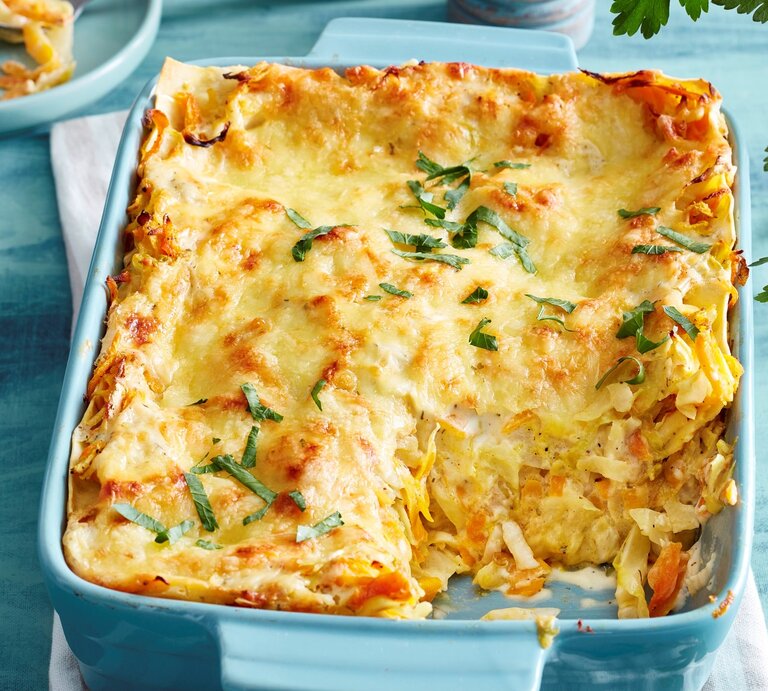 Blaue Ofenform mit angeschnittener Gemüse-Lasagne, Geschirr und Kräuter im blauen Hintergrund. | © EAT CLUB / Isabell Triemer
