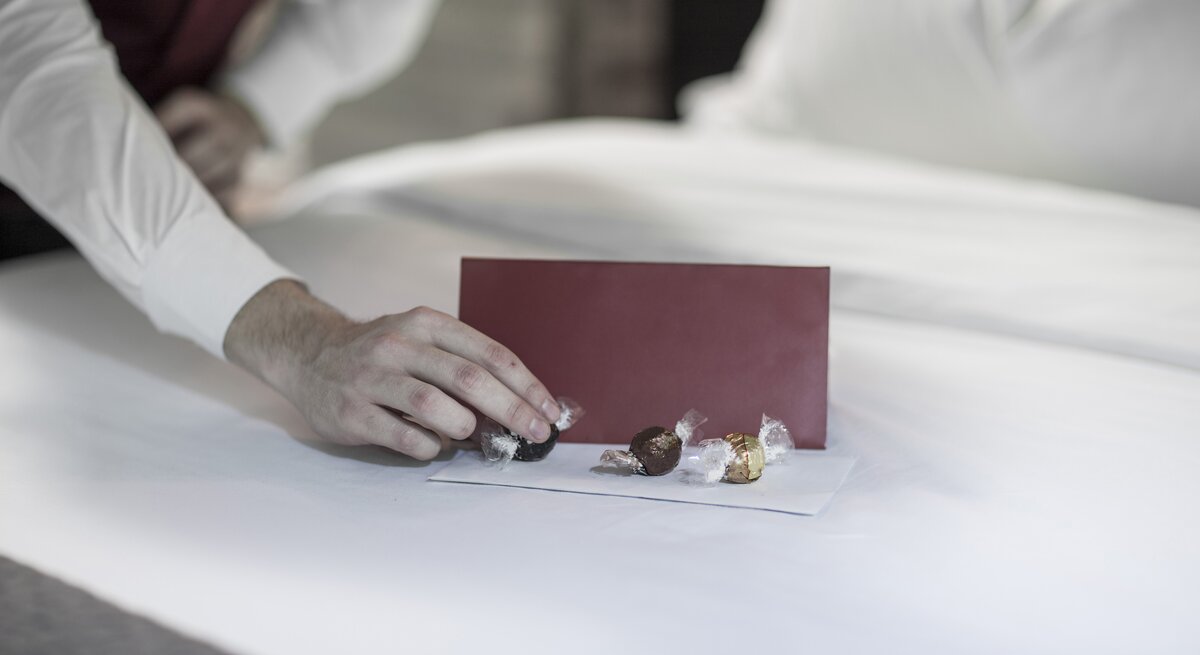Eine Person legt Pralinen auf das Hotelbett.