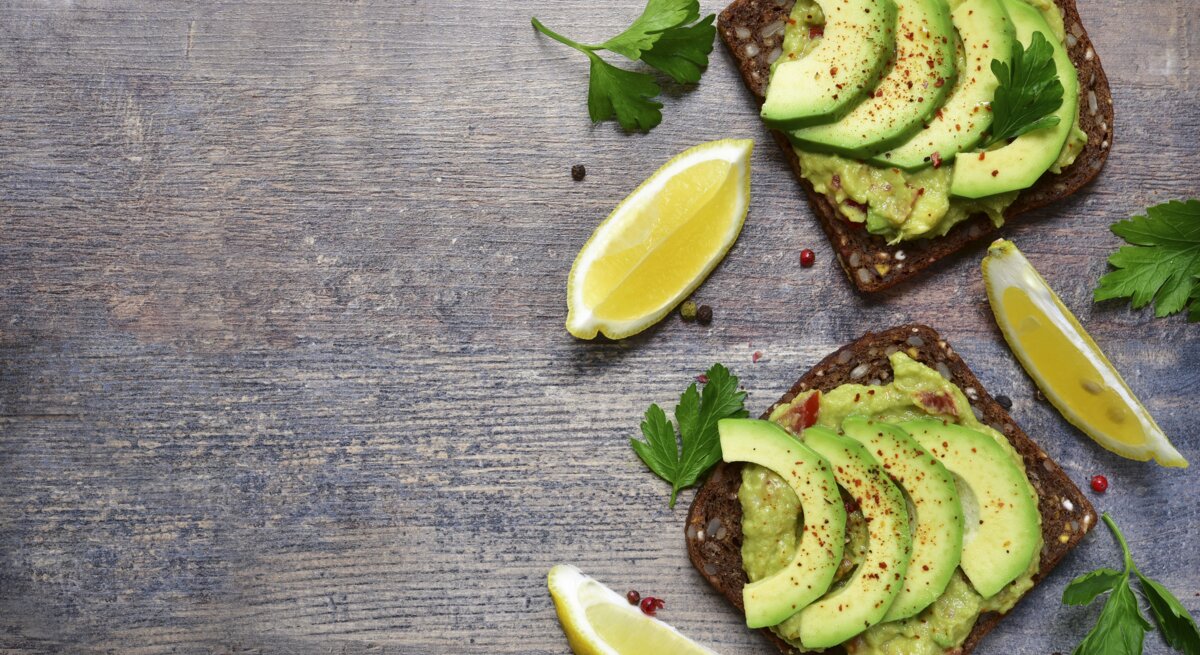 Zwei dunkle Brotscheiben mit Avocados belegt direkt von oben auf einem dunklen Tisch fotografiert.
