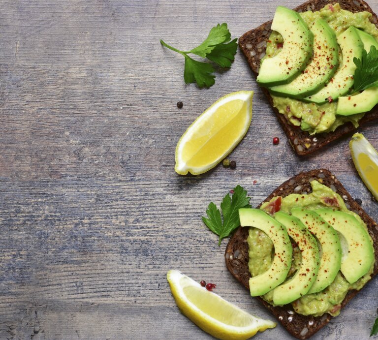 Zwei dunkle Brotscheiben mit Avocados belegt direkt von oben auf einem dunklen Tisch fotografiert. | © iStock/Lilechka75 