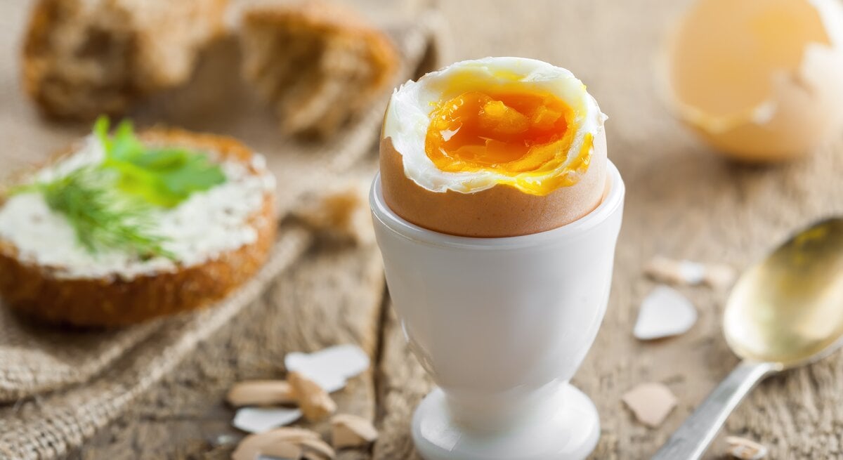 Geköpftes Frühstücksei in weißem Eierbecher auf Holz. 
