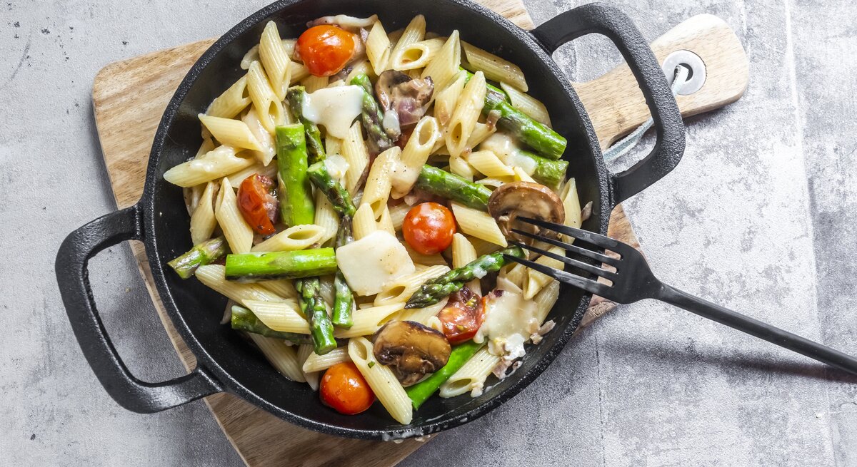 Spargel-Pasta-Pfanne mit Parmesan & Pilzen auf Holzbrett.
