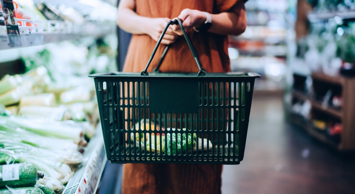 Vegan Food Award 2021: Eine Frau im Supermarkt hält einen Einkaufskorb und steht neben einem Gemüseregal.