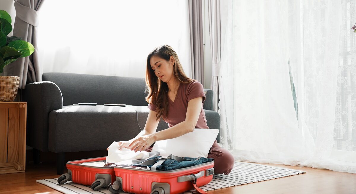 Eine Frau sitzt auf dem Boden und packt ihren Handgepäckskoffer.