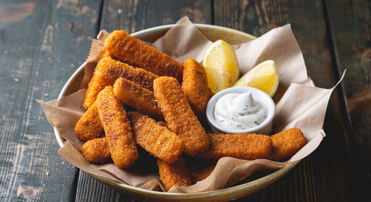 Ein Teller mit veganen Fischstäbchen, einer Schale Mayo und einer Zitronenspalte.