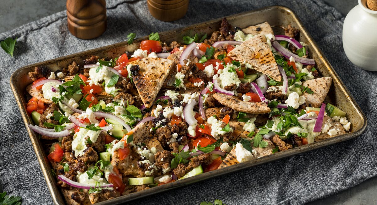 Gewürztes Hackfleisch mit Pita-Dreiecken und frischem Gemüse auf einem metallischen Backblech.