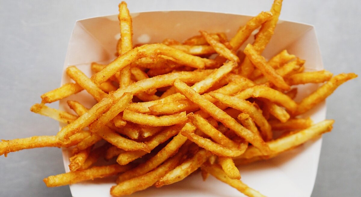 Eine weiße Schale mit knusprigen Pommes auf einem grauen Tisch.