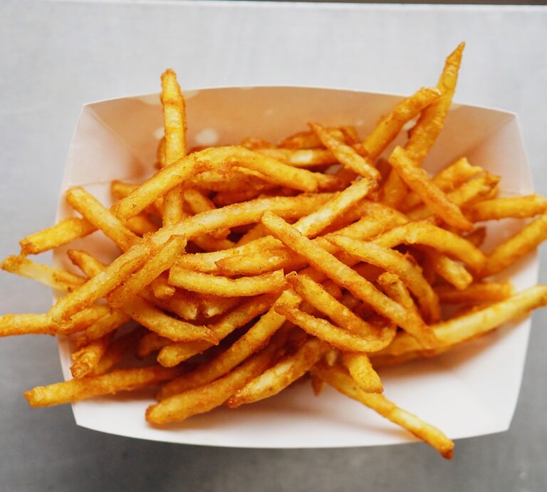 Eine weiße Schale mit knusprigen Pommes auf einem grauen Tisch. | © Gettyimages/ Mark Tan / EyeEm