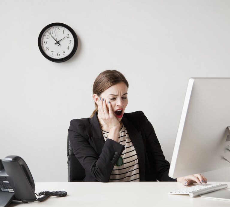 Müde Frau sitzt an Schreibtisch und gähnt | © Getty Images/	Jessica Peterson