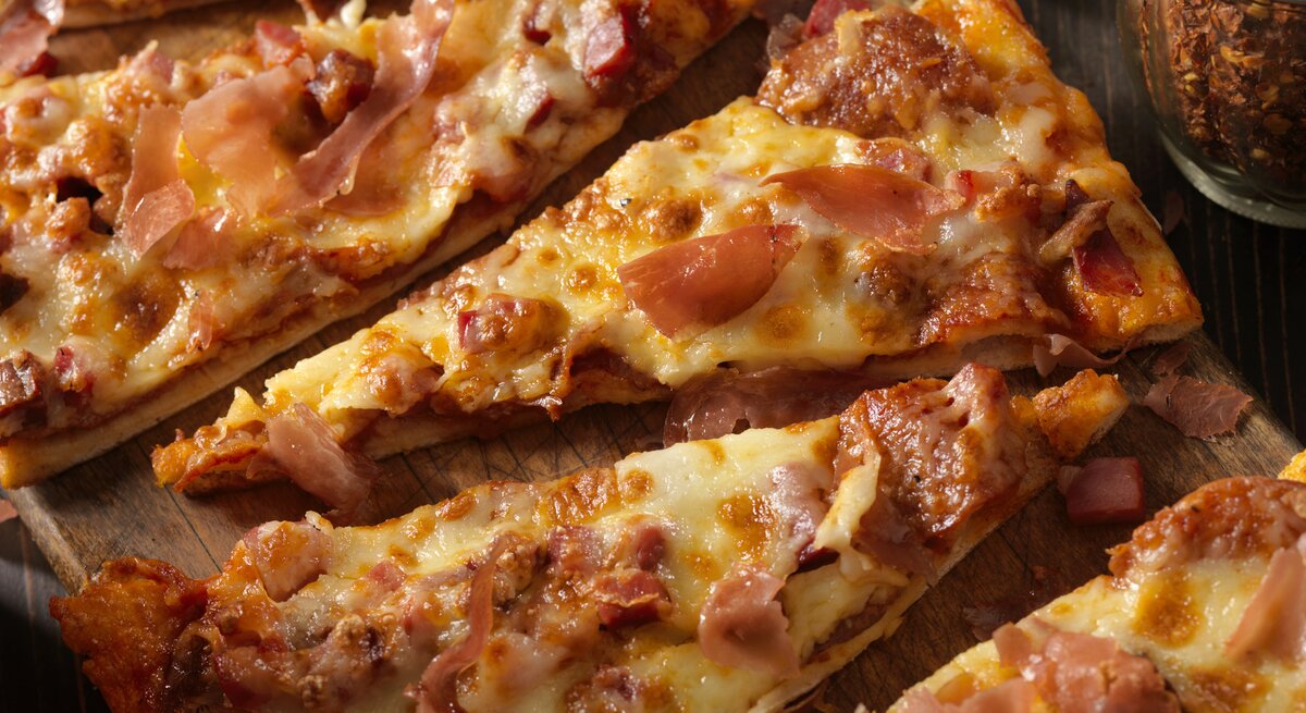 Pizza-Stücke mit Schinken, Salami und Käse auf Holzbrett.
