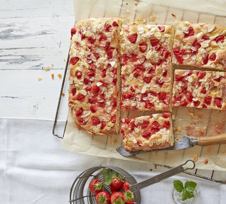 Der Kuchen auf einem hellen Holzbrett und hellem Tisch in Stücke geschnitten. Alles direkt von oben fotografiert. | © StockFood / Jalag / Hoersch, Julia