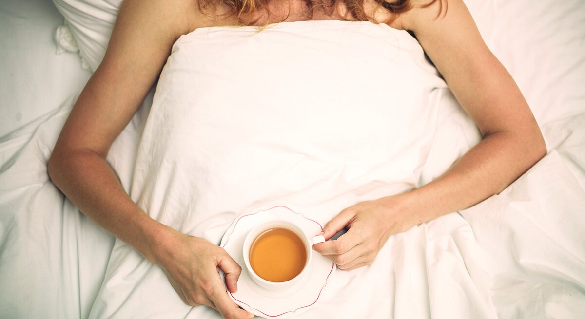 Frau mit einer Tasse Tee liegt im Bett