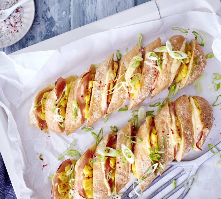 Hasselback-Baguette Hawaii auf einem Backblech mit weißem Backpapier. | © EAT CLUB/Isabell Triemer