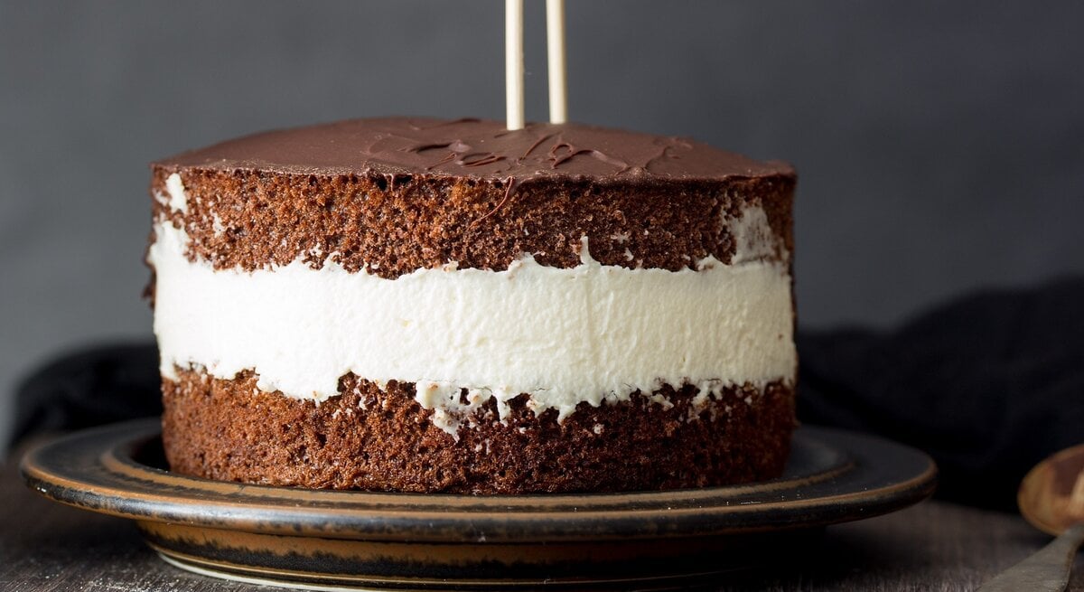 Die Torte auf einem dunkelbraunen Teller und dunklem Hintergrund mit zwei Mikadostäbchen in der Torte. Daneben ein Löffel und eine schwarze Tischdecke.