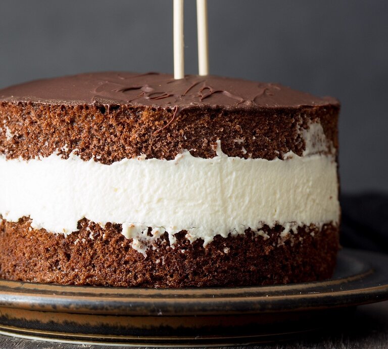 Die Torte auf einem dunkelbraunen Teller und dunklem Hintergrund mit zwei Mikadostäbchen in der Torte. Daneben ein Löffel und eine schwarze Tischdecke. | © Shutterstock/ yari2000