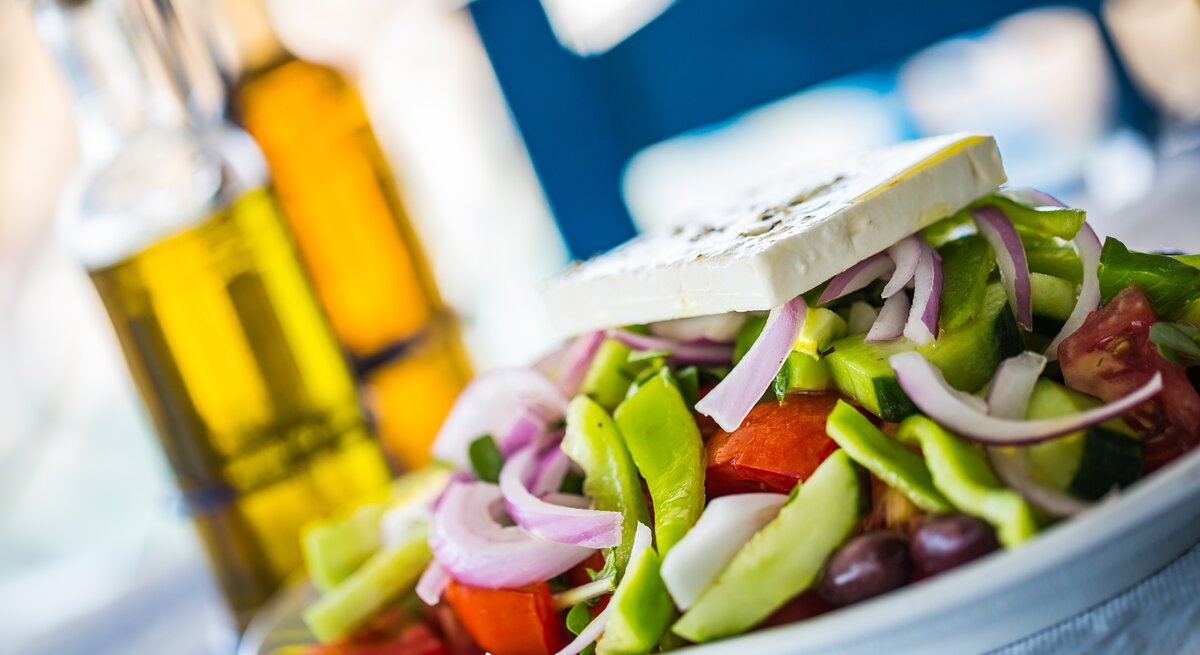Ein mit Feta garnierter griechischer Salat auf einem Teller. 