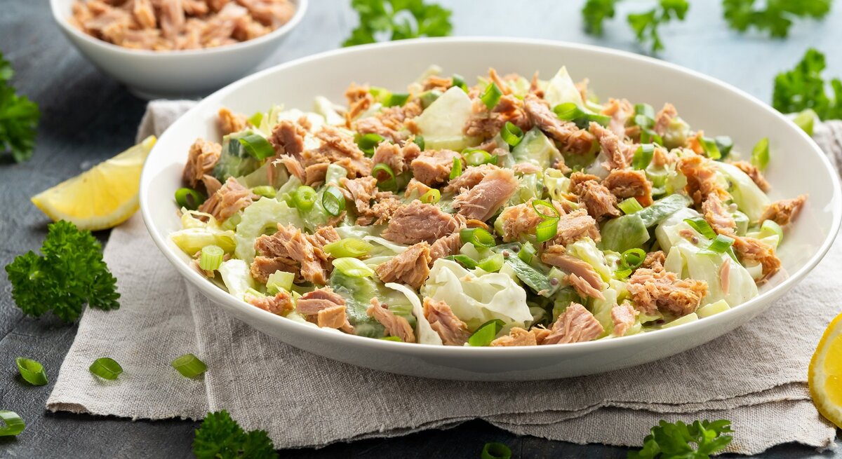 Eine flache Schale mit dem Salat auf grauem Untergrund. Daneben frische Zitronenecken und Petersilie.