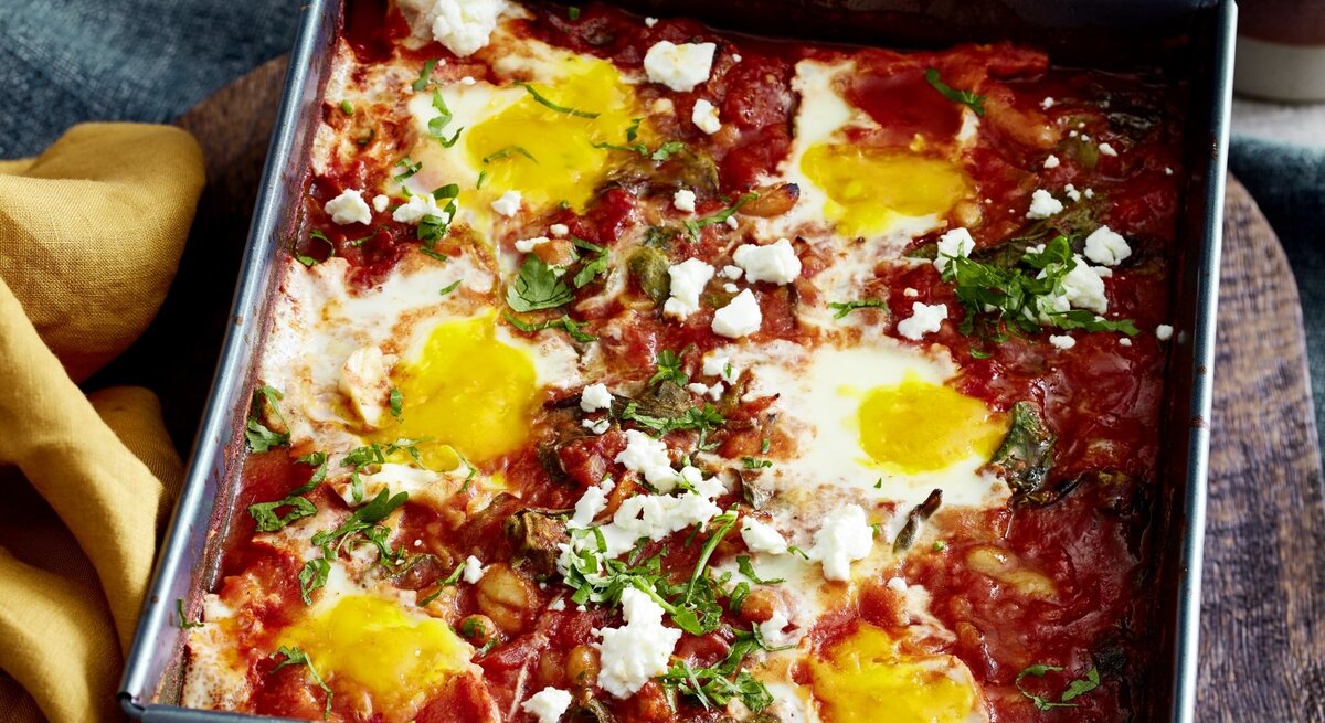 In einer Auflaufform ist ein Ofen-Shakshuka mit Spinat angerichtet. Es ist mit Petersilie bestreut. 