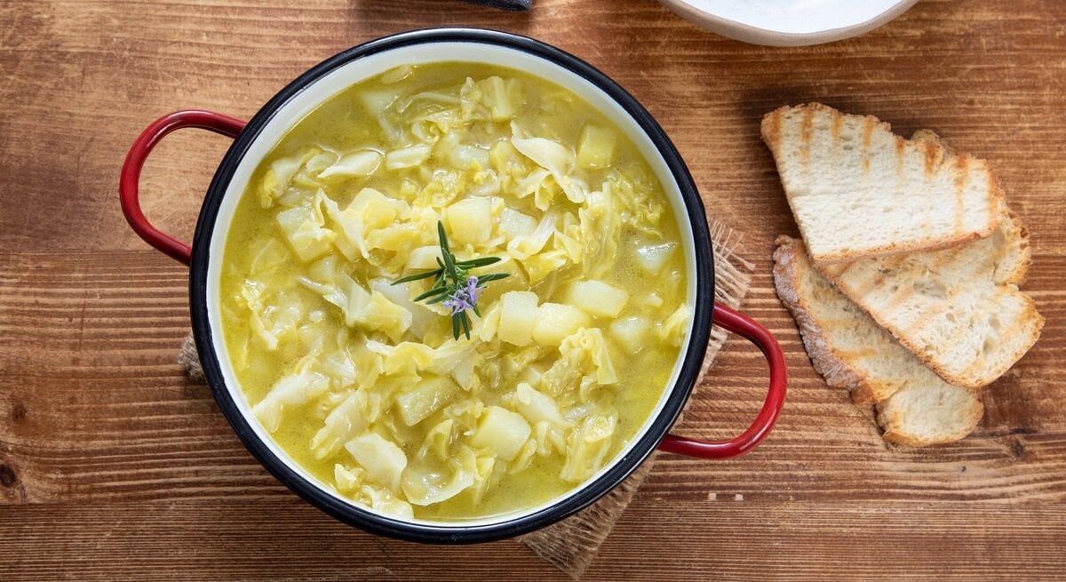 Ein Kartoffel-Weißkohl-Eintopf auf einem Holztisch mit zwei Brotscheiben.