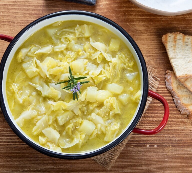 Ein Kartoffel-Weißkohl-Eintopf auf einem Holztisch mit zwei Brotscheiben. | © Shutterstock/ denio109