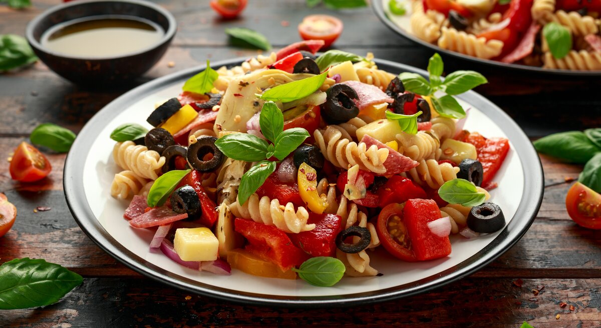 Antipasti-Nudelsalat mit Artischocken, Oliven, Salami, Käse und Basilikum.