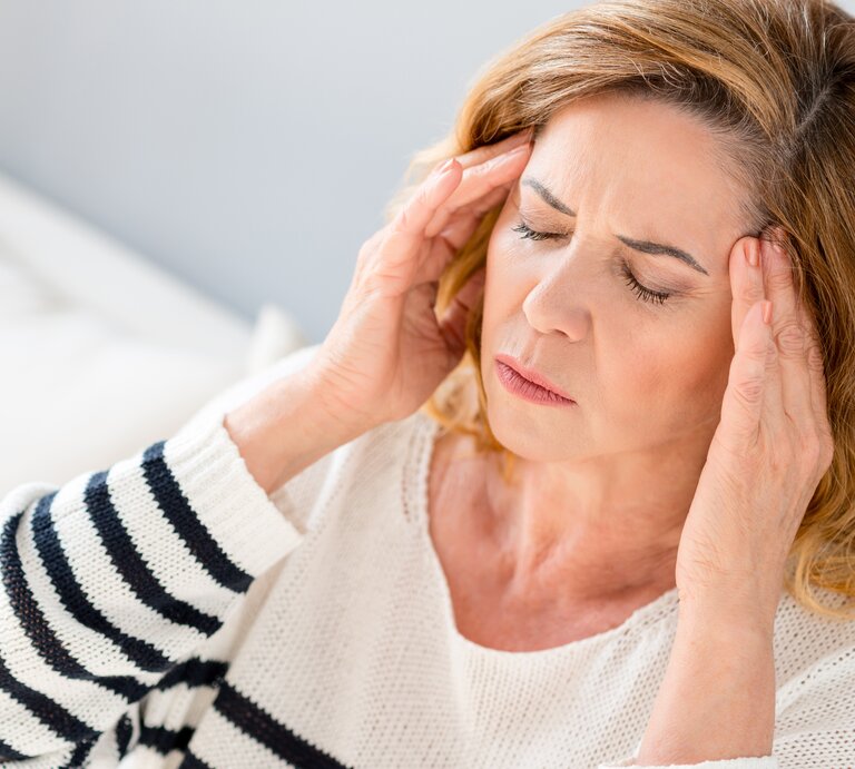 Eine Frau fasst sich bei Kopfschmerzen an die Schläfen und verzieht das Gesicht im Schmerz. | © iStock/YakobchukOlena