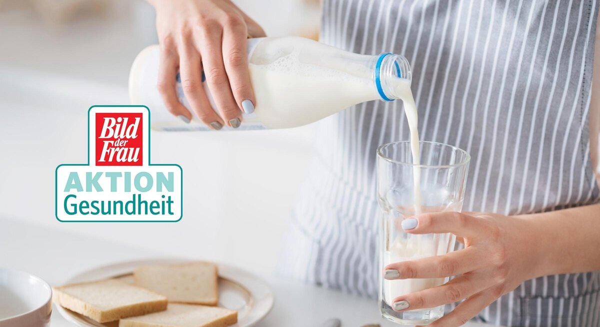 Eine Frau im gestreiften Oberteil gießt frische Milch aus einer Glasflasche in ein klares Glas. Die Szene spielt in einer hellen Küche, was auf eine alltägliche Haushaltstätigkeit hindeutet. Im Hintergrund ist ein Teller mit Scheiben Weißbrot und eine Schale zu sehen, was auf ein bevorstehendes Frühstück schließen lässt. Auf dem Bild ist ebenfalls das "Bild der Frau AKTION Gesundheit" Logo zu erkennen. Die gepflegten Hände der Frau und die sorgfältige Ausführung der Handlung vermitteln ein Gefühl von Fürsorge und Gesundheitsbewusstsein.