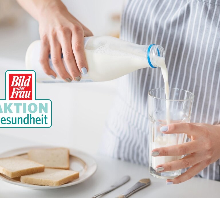 Eine Frau im gestreiften Oberteil gießt frische Milch aus einer Glasflasche in ein klares Glas. Die Szene spielt in einer hellen Küche, was auf eine alltägliche Haushaltstätigkeit hindeutet. Im Hintergrund ist ein Teller mit Scheiben Weißbrot und eine Schale zu sehen, was auf ein bevorstehendes Frühstück schließen lässt. Auf dem Bild ist ebenfalls das "Bild der Frau AKTION Gesundheit" Logo zu erkennen. Die gepflegten Hände der Frau und die sorgfältige Ausführung der Handlung vermitteln ein Gefühl von Fürsorge und Gesundheitsbewusstsein. | © iStock/Zinkevych [M]