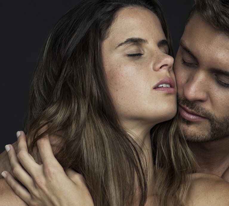 Ein Mann und eine Frau in einer intimen Umarmung, wobei der Mann seine Wange sanft an die der Frau drückt und beide die Augen geschlossen haben, was ein Gefühl von Nähe und Zärtlichkeit vermittelt. | © Getty Images/PhotoAlto/Frederic Cirou