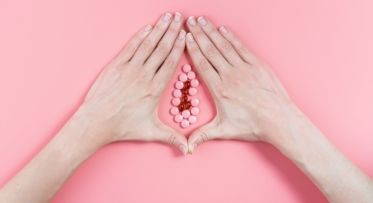 Zwei Frauenhände umschließen vor einem rosa Hintergrund eine Ansammlung von Pillen, so dass das Gebilde aussieht wie eine Vagina.