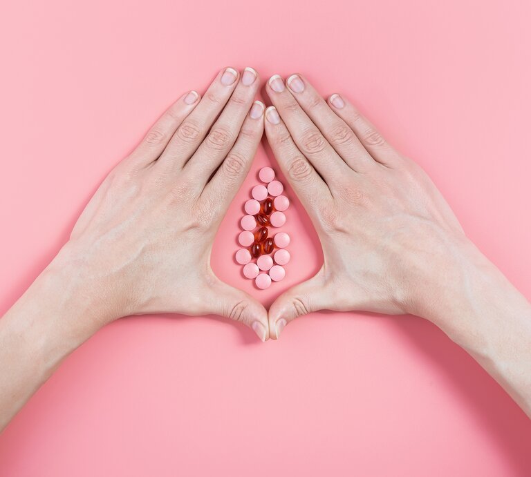 Zwei Frauenhände umschließen vor einem rosa Hintergrund eine Ansammlung von Pillen, so dass das Gebilde aussieht wie eine Vagina. | © Shutterstock / Mikhaylovskiy