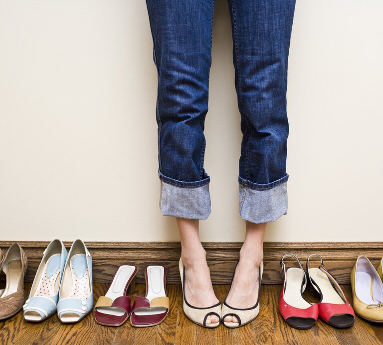Viele Schuhe in einer Reihe aufgestellt, dazwischen die Beine und Füße einer Frau.  | © iStock / michellegibson