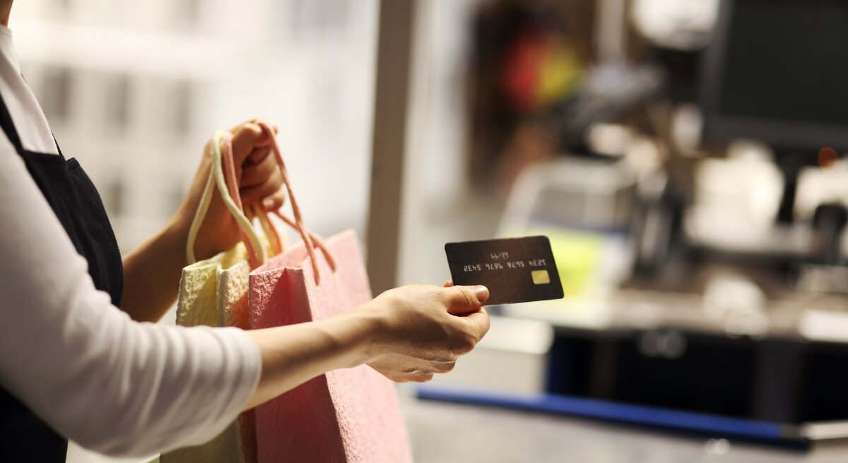 Ein Frauenarm, der Shoppingtüten und eine Kreditkarte hält