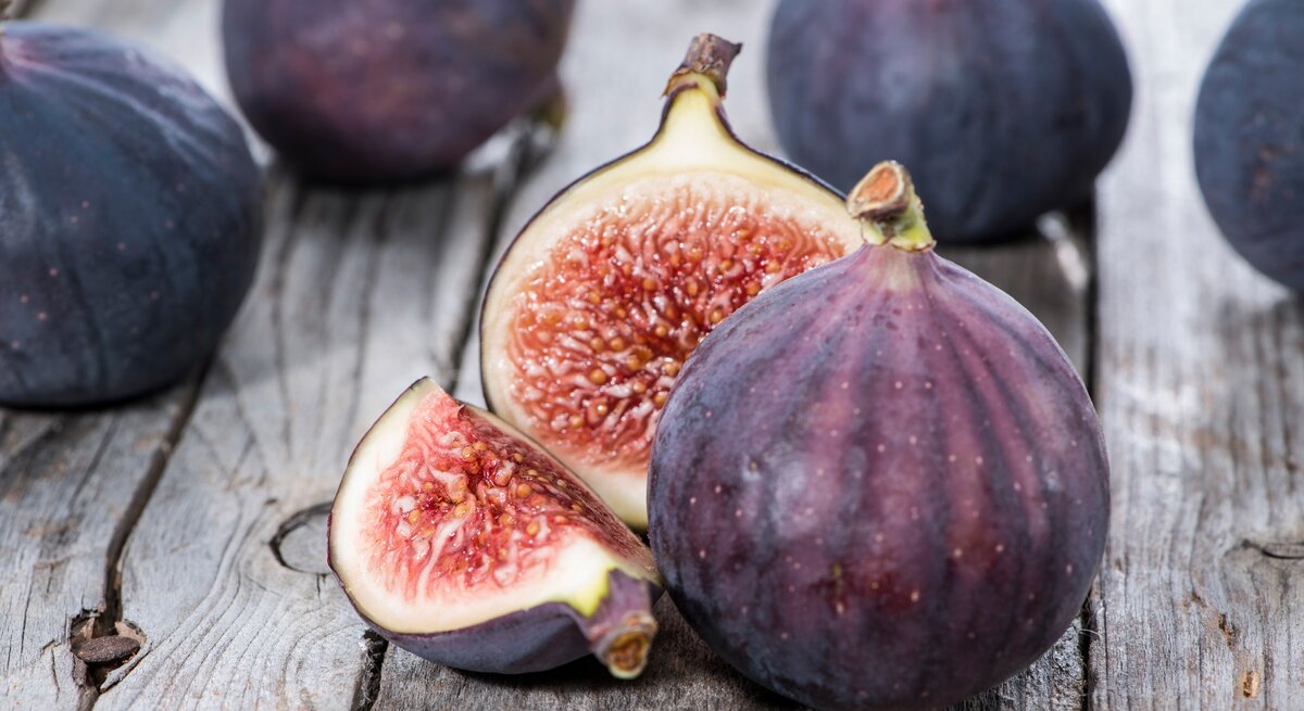 Frontalsicht: Ganze und angeschnittene violette Feigen liegen auf einem Holztisch