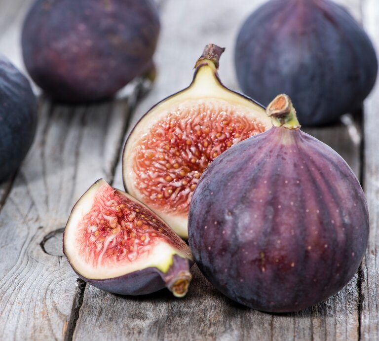 Frontalsicht: Ganze und angeschnittene violette Feigen liegen auf einem Holztisch | © Shutterstock / HandmadePictures