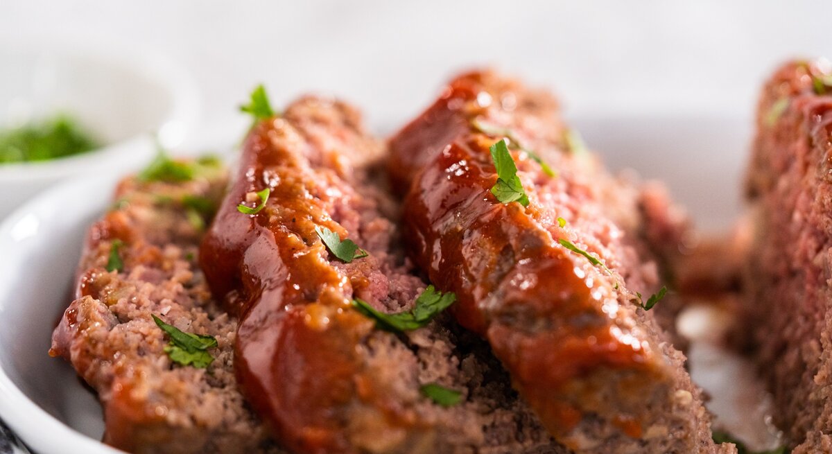 Hackbraten mit Schmorgemüse und Petersilie bestreut. Nah und in Scheiben geschnitten auf weißem Teller und mit weißem Hintergrund fotografiert