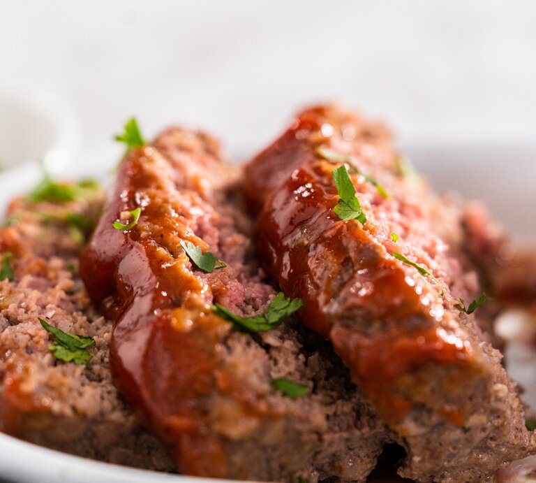 Hackbraten mit Schmorgemüse und Petersilie bestreut. Nah und in Scheiben geschnitten auf weißem Teller und mit weißem Hintergrund fotografiert | © Adobe Stock/ arinahabich