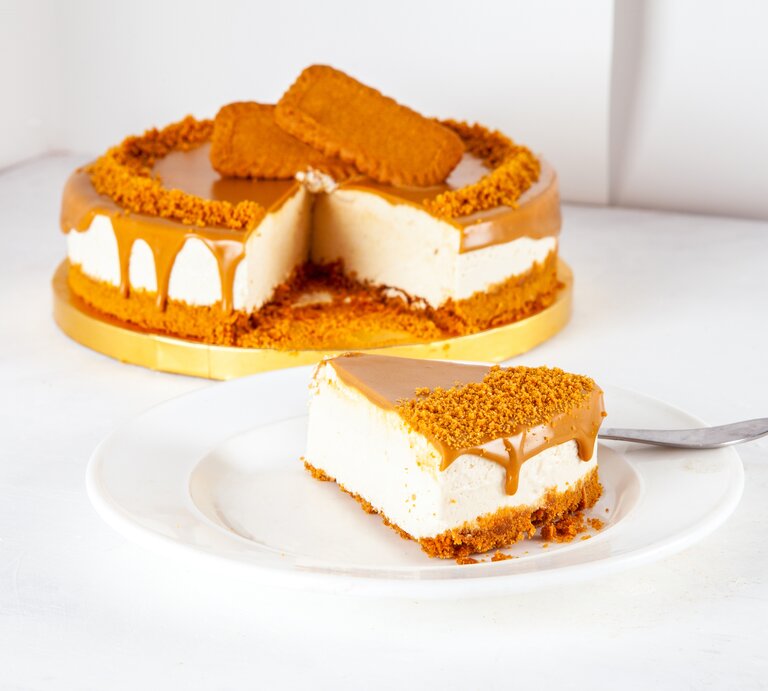 Goldene Tortenplatte, darauf ein Käsekuchen mit Lotus-Keksen. Ein Stück wurde herausgeschnitten und auf einem Teller angerichtet.  | © shutterstock/razum