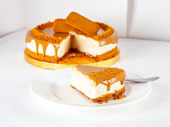 Goldene Tortenplatte, darauf ein Käsekuchen mit Lotus-Keksen. Ein Stück wurde herausgeschnitten und auf einem Teller angerichtet.  | © shutterstock/razum