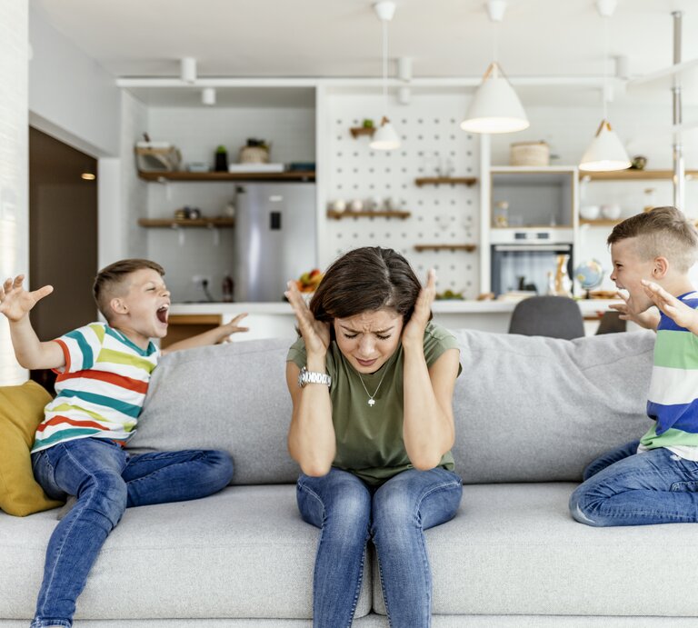 Kinder schreinen sich gegenseitig an. Mutter sitzt dazwischen und hält sich die Ohren zu. | © Getty Images/ljubaphoto