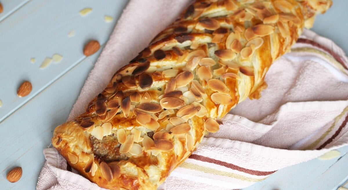 Ein Marzipan-Mandel-Strudel auf einem hellen Tisch mit rosa Tischdecke. Alles von schräg oben fotografiert.