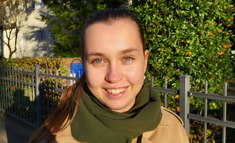 Porträtbild der Autorin Linda Pötzsch, die braune Haare hat und einen grünen Schal zusammen mit einem beigen Trenchcoat trägt. Sie lächelt dabei direkt in die Kamera. | © Linda Pötzsch