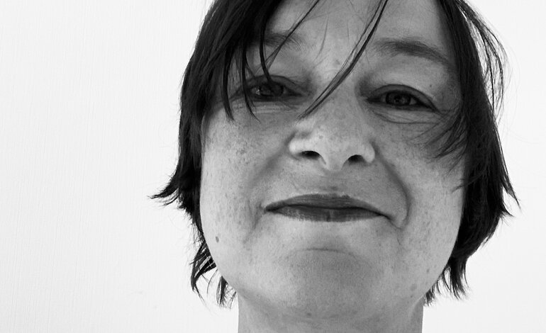 Schwarz-weiß Porträtfoto einer lächelnden Frau mit kurzen dunklen Haaren und einem schlichten Oberteil. | © privat