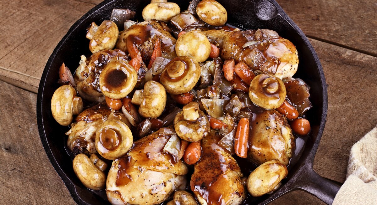Gusseiserne Pfanne auf Holz gefüllt mit Coq au vin samt Pilze und Fleisch. 